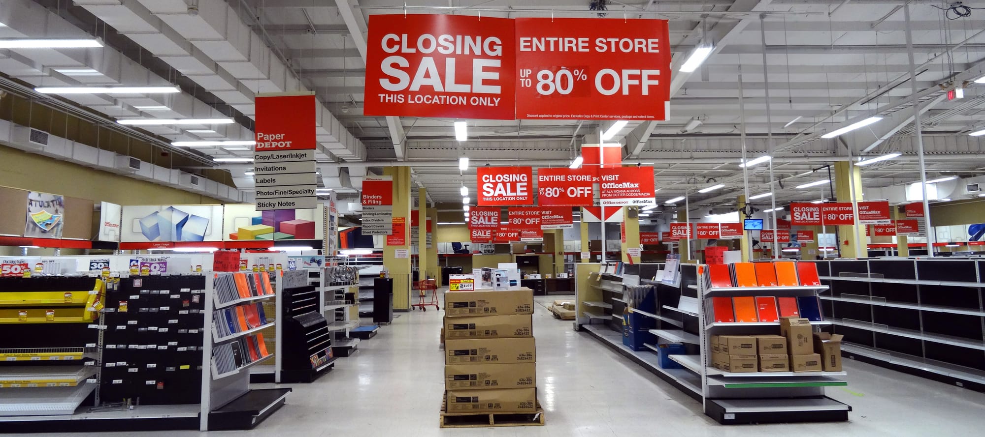 Photo of an office store with 'closing sale' signs displayed from the ceiling.