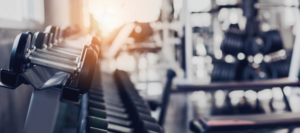 Image of a fitness center with dumbbells in the foreground. 