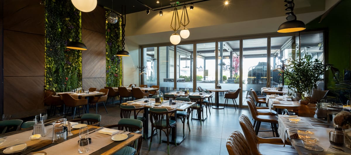 Modern empty restaurant interior with wood panel walls, plants, and tables with chairs.